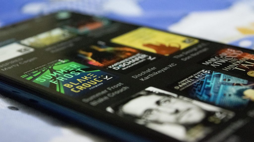 A photograph of my phone's digital library with fiction books like Dischafer and non-fiction books like Permanent Record in focus.